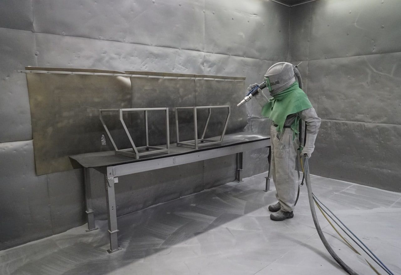 Strahlkabine, Mitarbeiter führt den Strahl über das Bauteil.